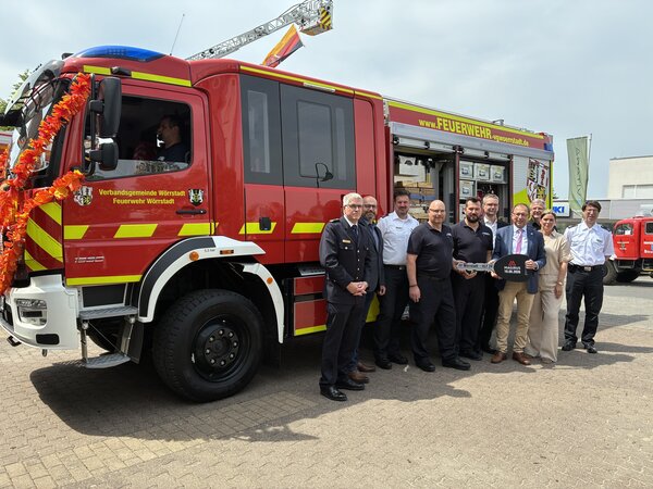 Vor einem Feuerwehrauto stehen viele Menschen. Das Auto ist neu und wurde der Feuerwehr gerade &uuml;bergeben. 