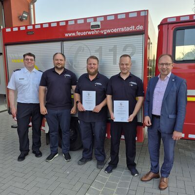 Mehrere M&auml;nner stehen vor einem Feuerwehrauto. 